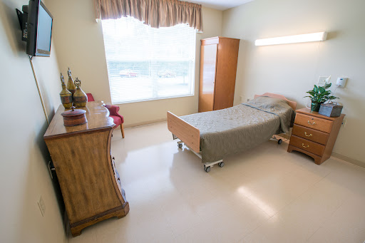 A well-lit hospital room featuring a single bed, a dresser, and a chair near the window.