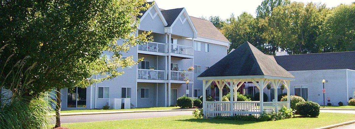 A residential apartment building with balconies and a nearby gazebo surrounded by greenery.