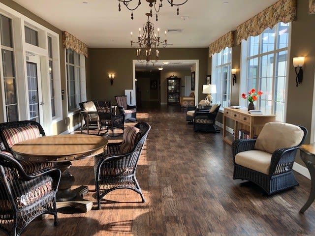 A cozy living room with multiple seating areas, large windows, and a chandelier accenting the hardwood floor.