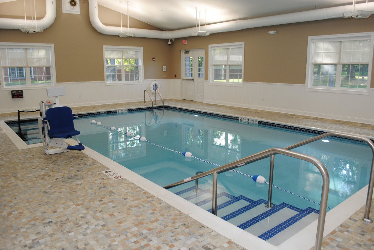 An indoor swimming pool with steps and a handrail, surrounded by windows.