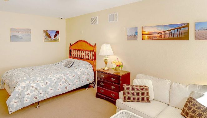 A cozy bedroom with a wooden bed, patterned bedding, a lamp on a dresser, and artwork on the walls.