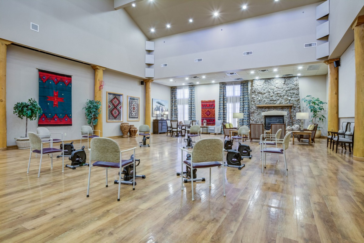 A spacious room with hardwood flooring, arranged chairs, large windows, and decorative artwork on the walls.