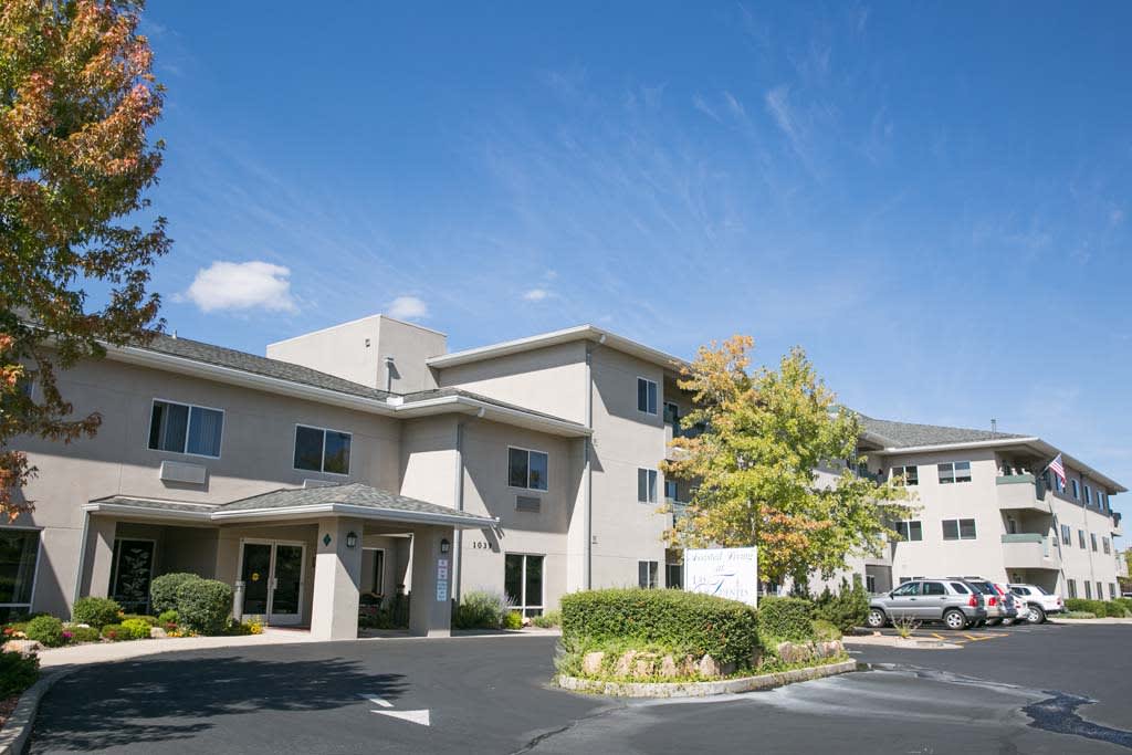 A residential building with a driveway and surrounding trees under a clear blue sky.
