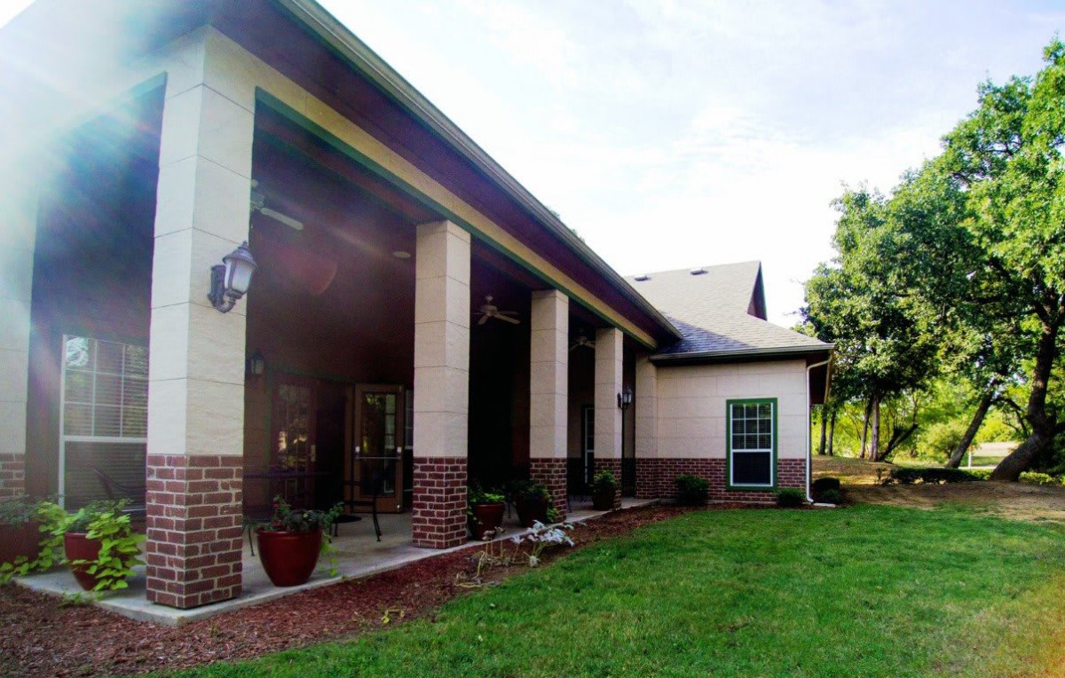 A view of a house exterior with brick and siding, featuring a spacious porch and lawn.