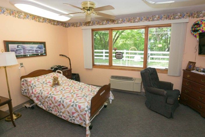 A cozy bedroom with a single bed, a recliner, and large windows overlooking greenery.