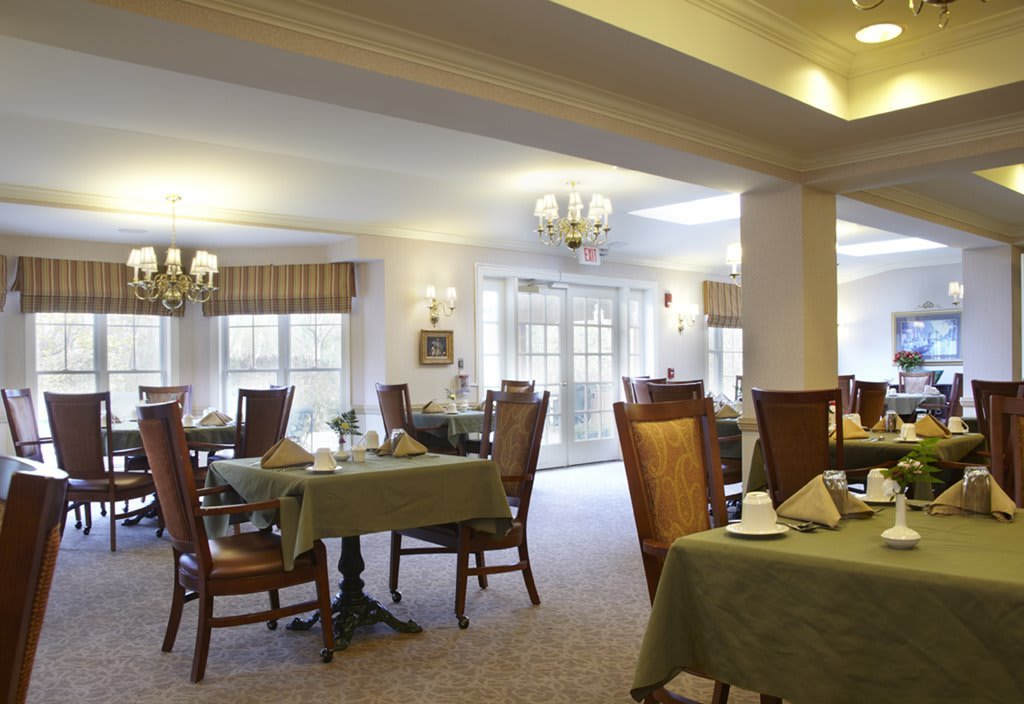 An elegant dining room with neatly arranged tables and chairs, illuminated by chandeliers.