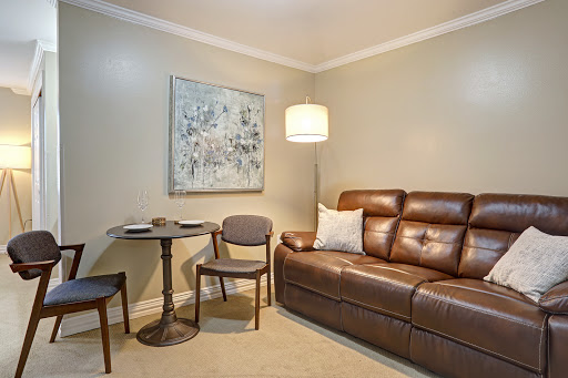A cozy living room setup featuring a brown sofa, a small table with two chairs, and an abstract artwork on the wall.