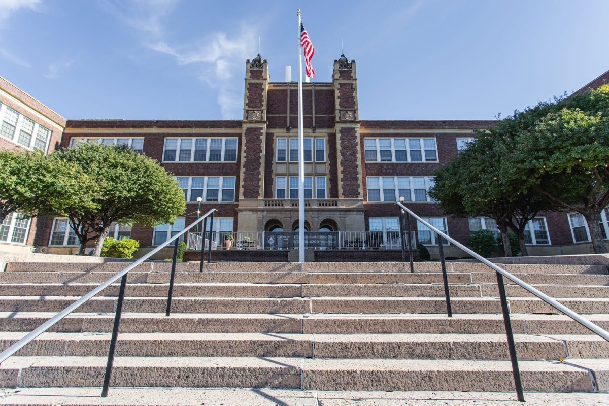 A classic school building with a flagpole, seen from the bottom of the entrance stairs.