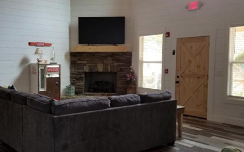 A cozy living room featuring a sofa, a stone fireplace with a television above it, and natural light coming through the window.