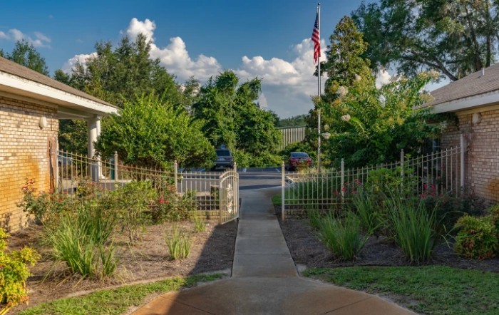 A sunny garden pathway leading to a flag with lush greenery and a clear sky.