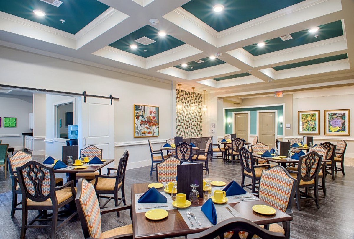 An elegant dining room setup with neatly arranged tables and chairs, featuring decorative ceiling lights and colorful table settings.