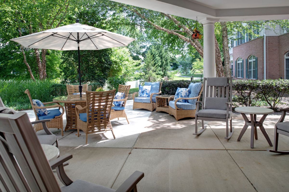 A cozy patio with comfortable seating and a dining area under a sun umbrella, surrounded by lush greenery.