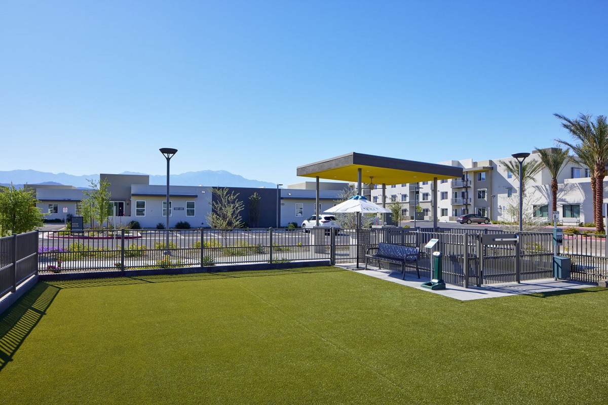 A modern outdoor playground with a shaded area, surrounded by buildings.