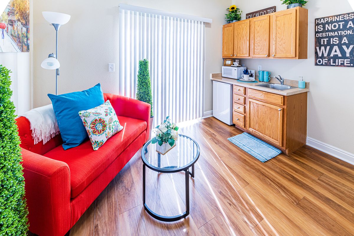 A brightly lit modern living space with a red sofa and kitchenette.