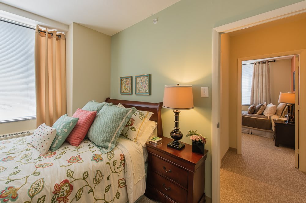 A cozy bedroom with floral bedding, colorful pillows, and a warm lamp on the nightstand.