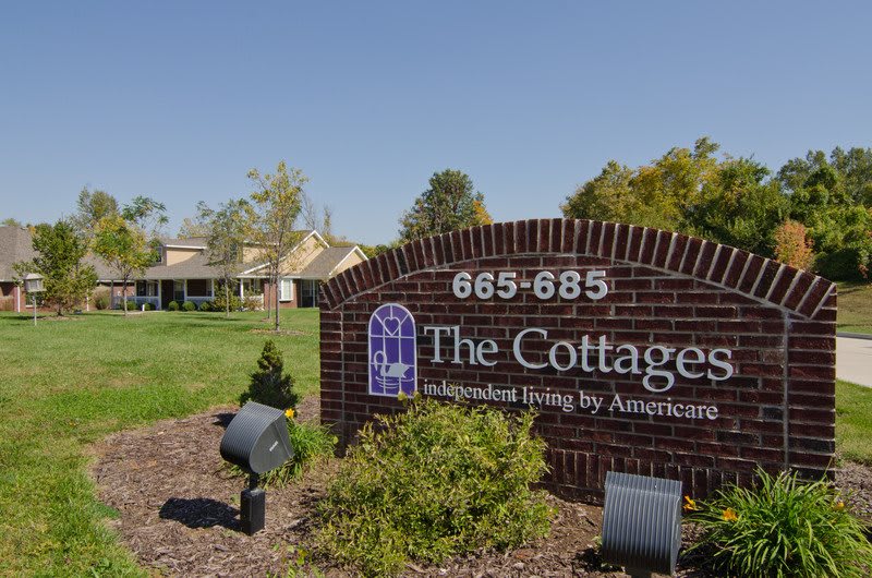 Image of 'The Cottages', an assisted living facility by Americare, featuring a brick sign with the complex in the background.