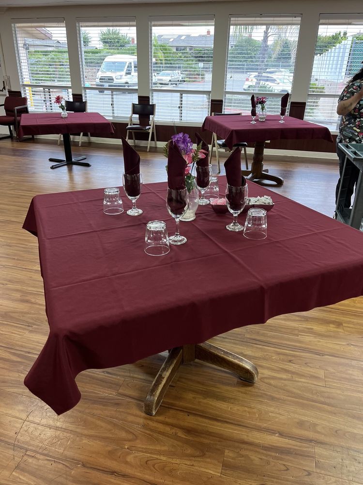 Elegantly set dining tables with maroon tablecloths and folded napkins in a restaurant.