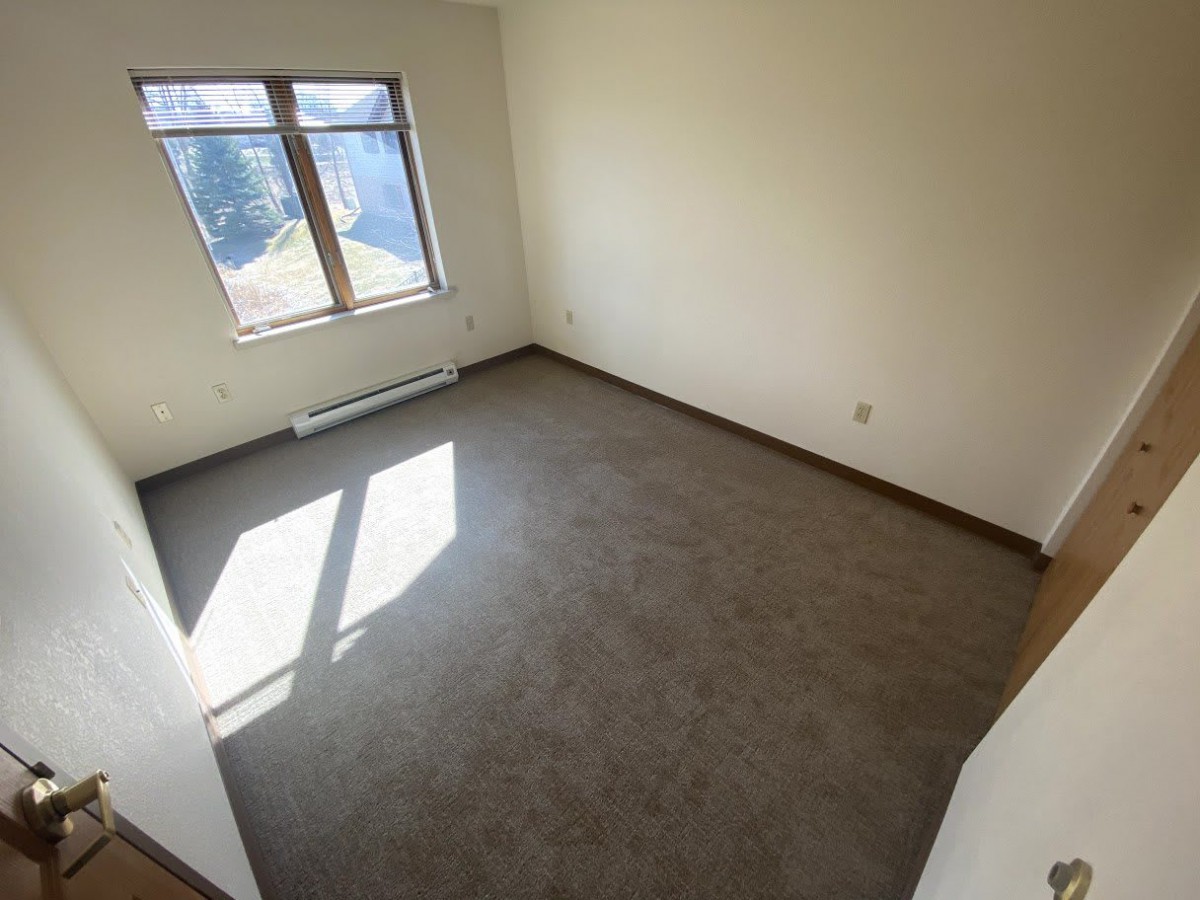 An empty room with a carpeted floor and sunlight streaming in through a window.