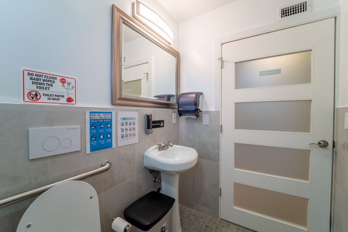 An accessible bathroom featuring a sink, mirror, handrail, and paper towel dispenser.