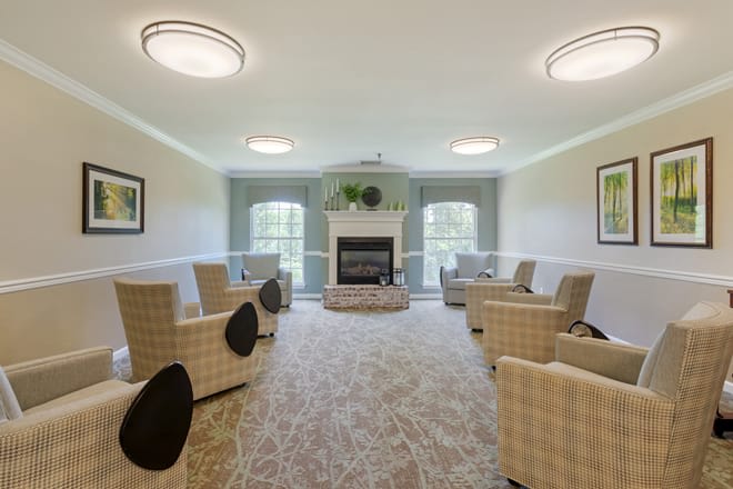 A cozy living room with a fireplace, surrounded by comfortable chairs and large windows.