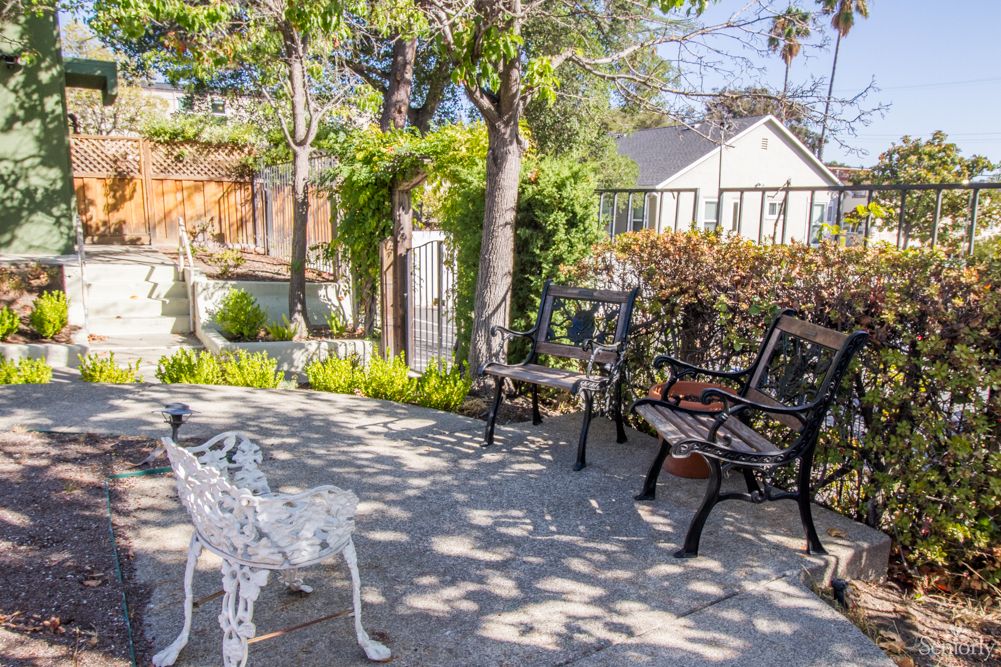 A serene outdoor patio area with benches and dappled sunlight filtering through the trees.
