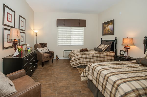 A cozy bedroom featuring twin beds with plaid bedding, a comfortable armchair, and warm lighting.