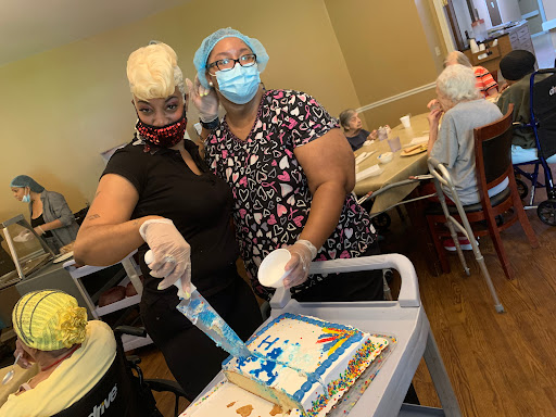 Two women preparing a cake for a celebration while wearing masks.