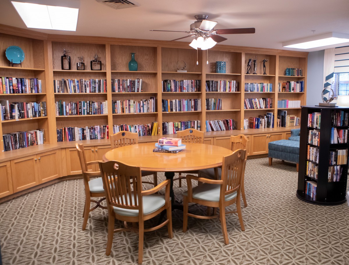 A cozy library corner with bookshelves and a round table surrounded by chairs.