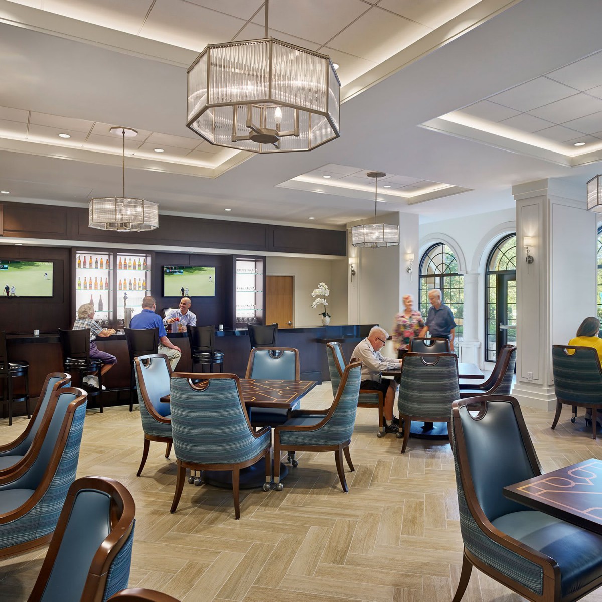 A modern restaurant interior with patrons dining, featuring elegant chandeliers and large windows.