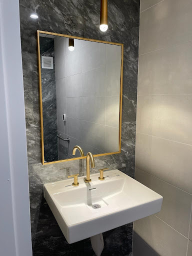 A stylish bathroom featuring a sleek sink with gold fixtures and a framed mirror against a marble backdrop.