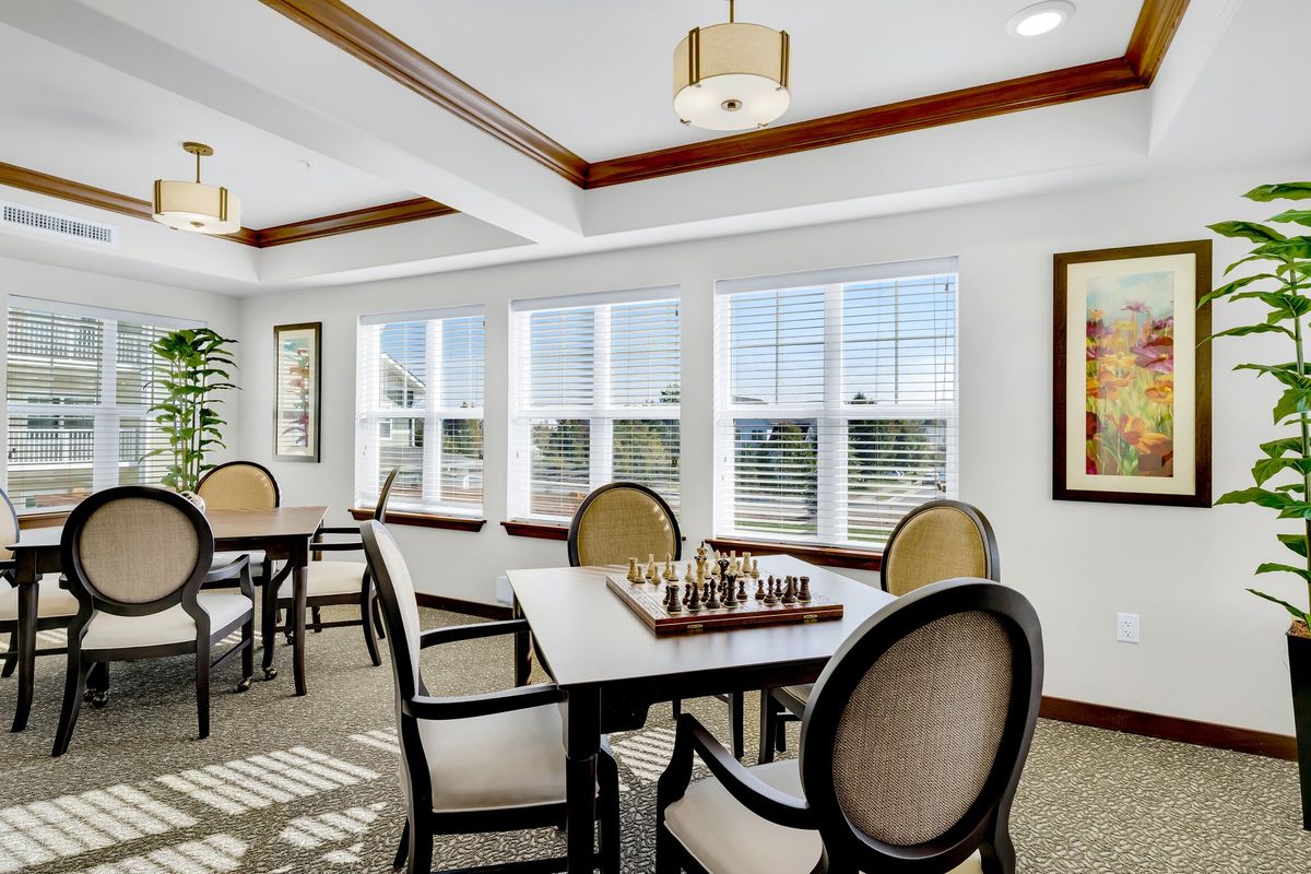 A well-lit room with multiple tables and chairs, featuring chessboards and large windows.