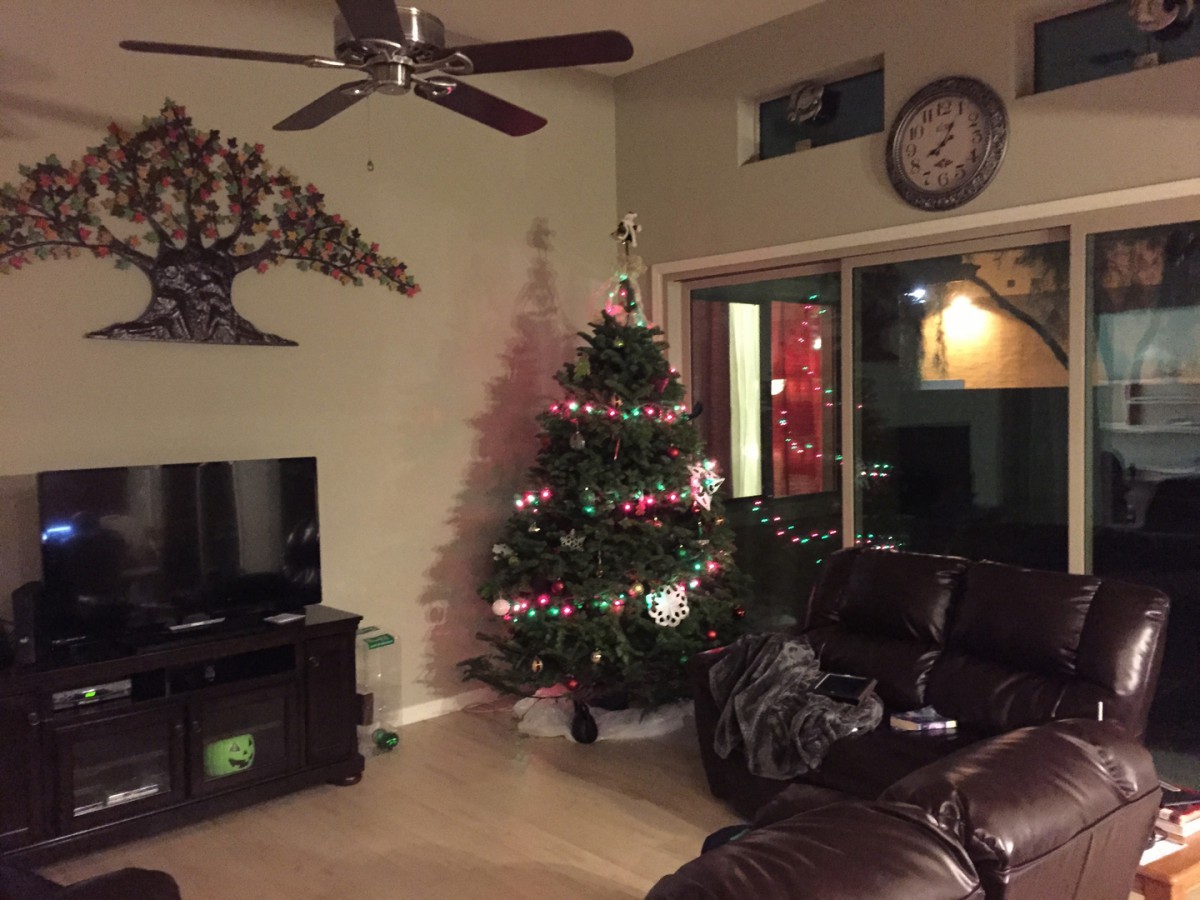 A cozy living room decorated for the holidays with a lit Christmas tree, comfortable seating, and a television.