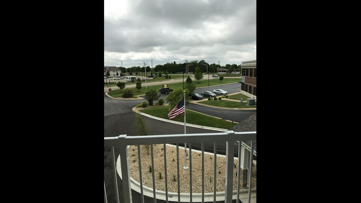 A view from a balcony overlooking an American flag in front of a parking lot and building on a cloudy day.