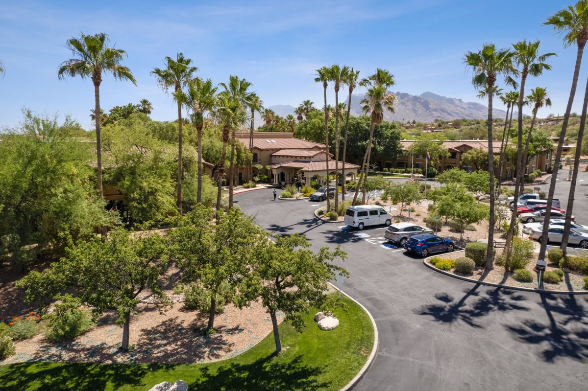 A desert resort with palm trees, a parking lot, and distant mountains under a clear blue sky.