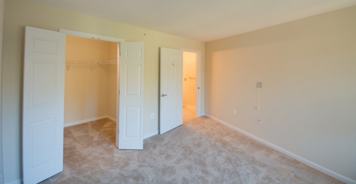 An empty bedroom with carpeted flooring, featuring a closet and open doors.