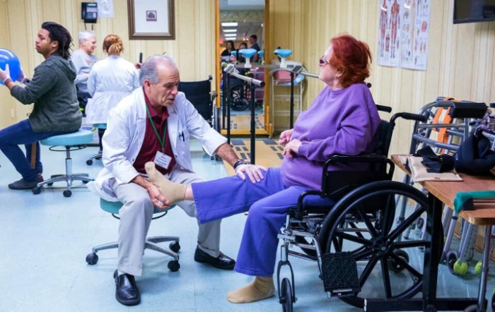 A doctor examines a patient's leg in a wheelchair at a clinic.