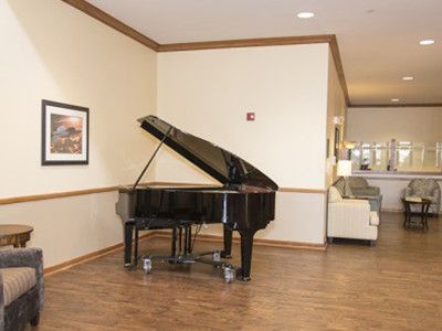 A grand piano in a lobby area with wood flooring and wall art.