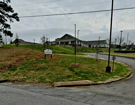 A view of a residential building with an open grassy area in the foreground under a cloudy sky.