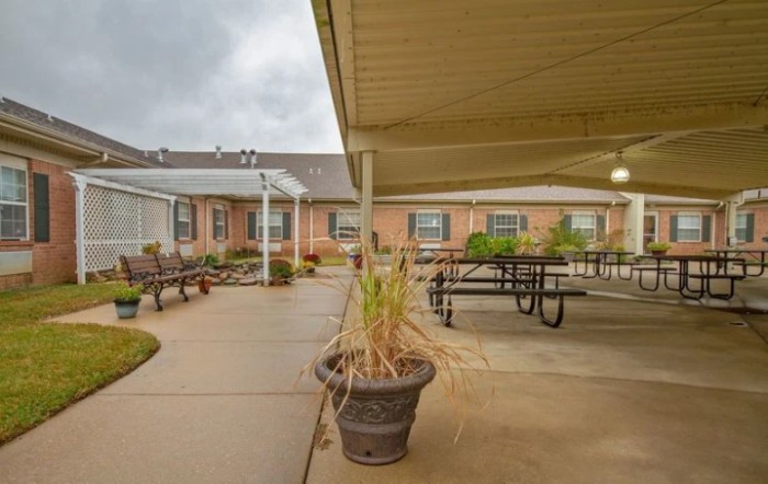 A covered outdoor patio area with benches, tables, and potted plants under an overcast sky.