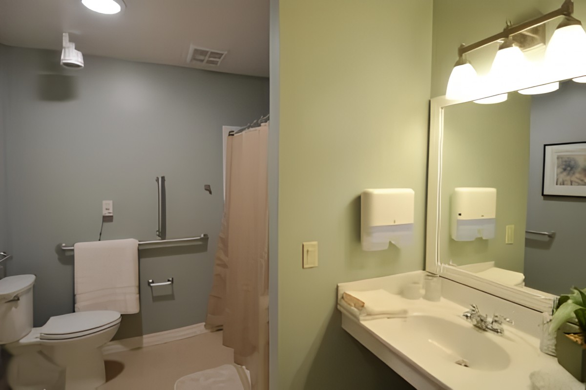 A clean, handicap-accessible bathroom with a sink and mirror, featuring green walls and adequate lighting.