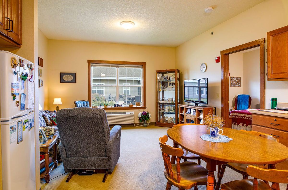 A cozy living room with a dining area, featuring a comfortable chair, bookshelves, and a TV.