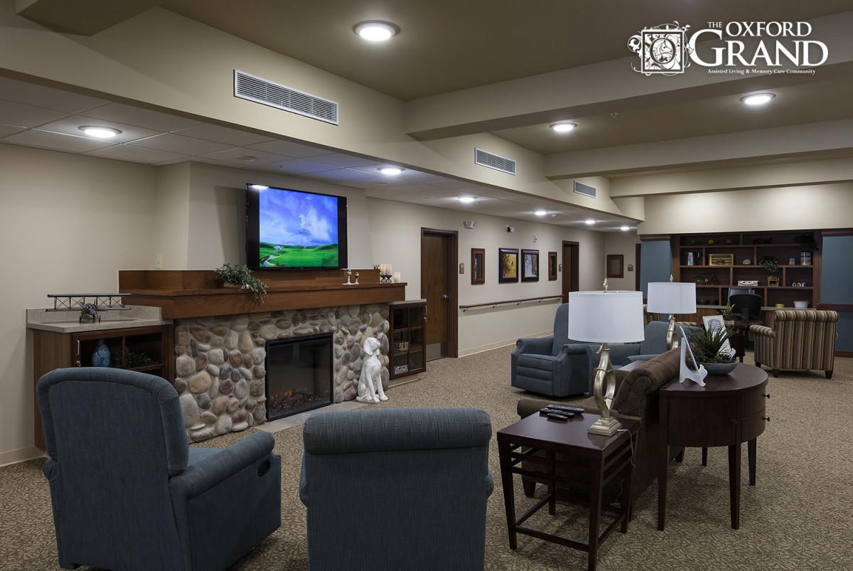 A cozy living room with a fireplace and television, featuring comfortable seating and bookshelves.