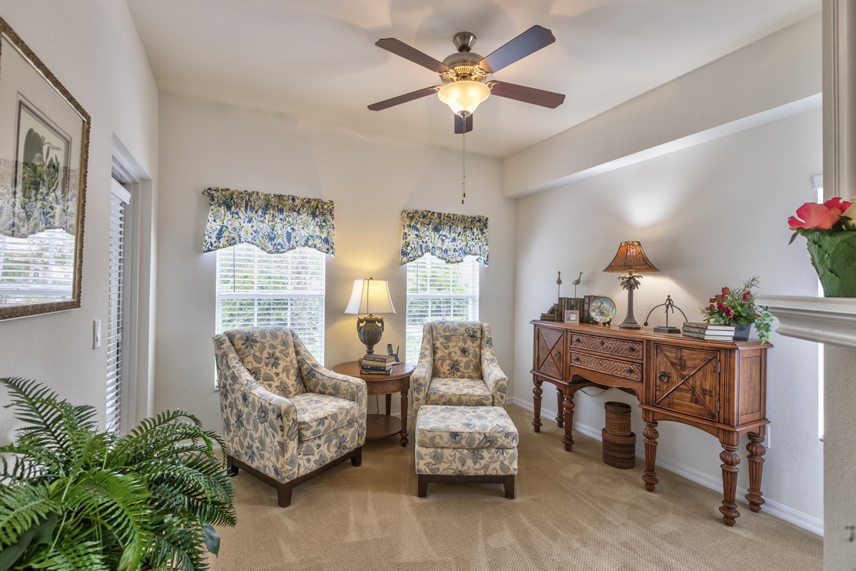 A cozy living room with floral-patterned chairs, a side table, and a ceiling fan.