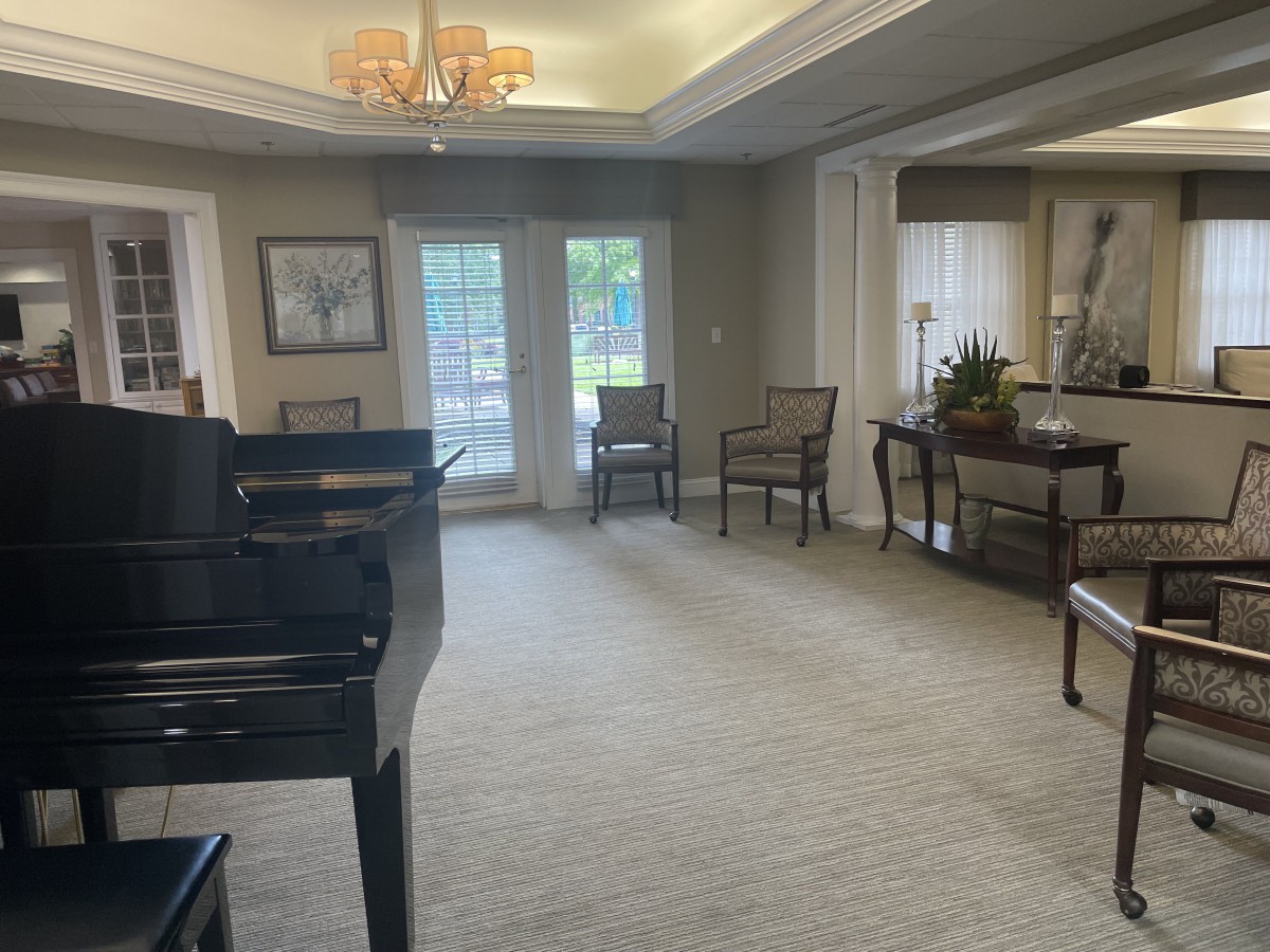 A spacious living room with a grand piano, elegant furniture, and large windows.