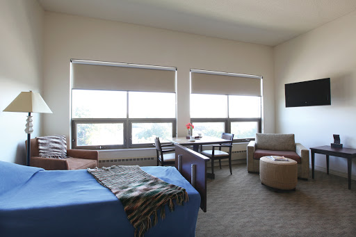 A well-lit and modern room featuring large windows, comfortable seating, and a neatly made bed.
