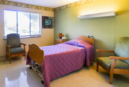 A cozy hospital room featuring a single bed with purple bedding, a small nightstand, and a comfortable chair.