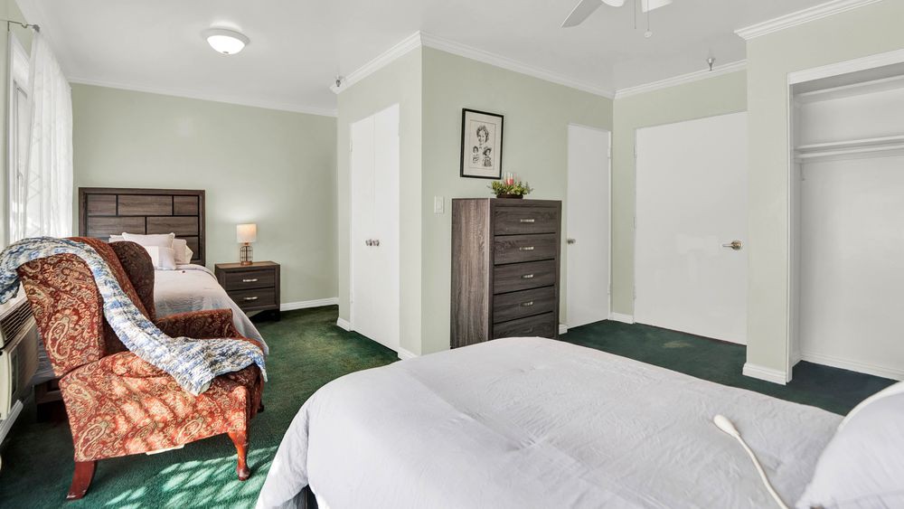 A cozy bedroom with a bed, dresser, and nightstand on green carpeting.