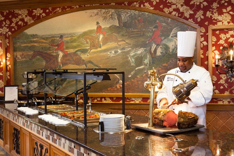 A chef at a restaurant carving meat at a buffet station.
