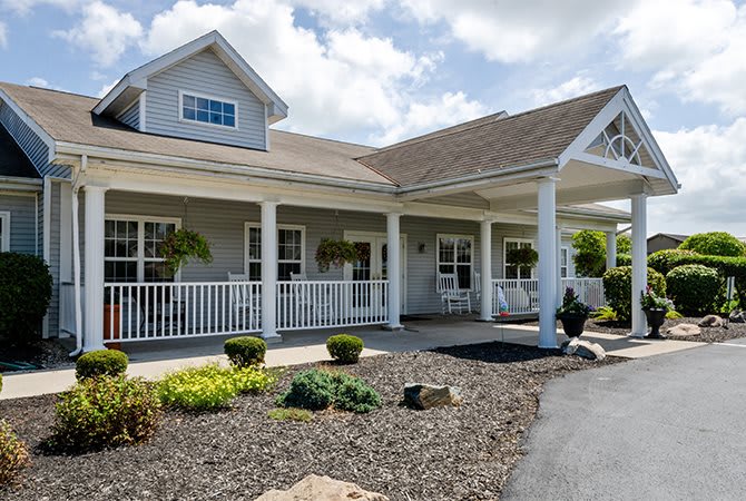 A charming residential home with a front porch and landscaped yard on a sunny day.