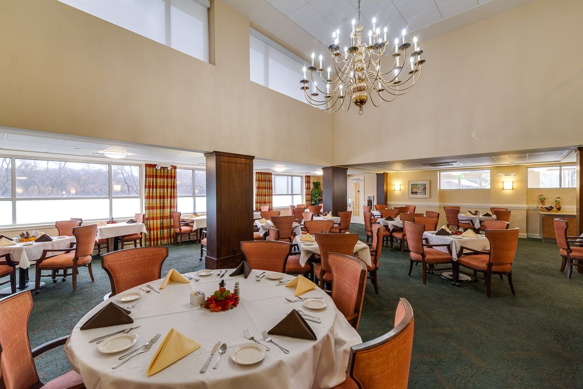 An elegant dining room with a chandelier, set with tables and chairs prepared for guests.